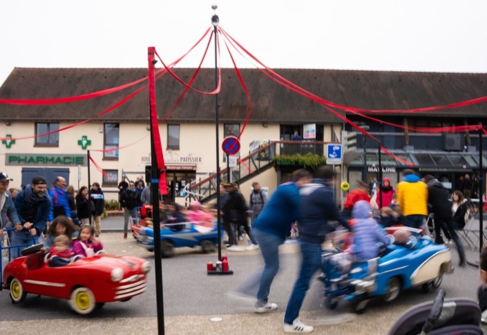 Les parents poussant les voitures du manège avec leurs enfants dedans sur une place publique.