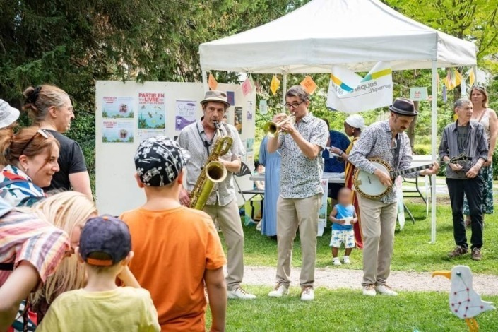Le trio Lil'Brass Band parcourant un parc public à Epernay lors du festival Voi(x)là l'été 2024 tout en jouant leur répertoire musical.